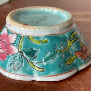 Puede incluir: Un peque&ntilde;o cuenco de porcelana con bordes festoneados, con un esmalte turquesa y un dise&ntilde;o floral. El cuenco tiene un borde blanco y las palabras "CHINA" est&aacute;n impresas en la parte inferior.