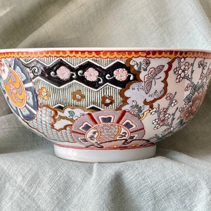 May include: A large white ceramic bowl with a colorful floral and geometric design. The bowl has a wide rim and a rounded base.