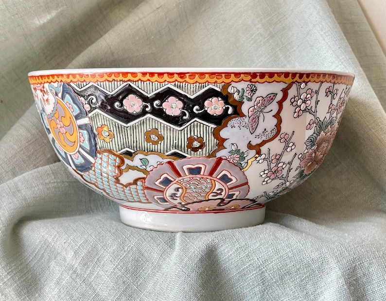 May include: A large white ceramic bowl with a colorful floral and geometric design. The bowl has a wide rim and a rounded base.