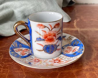 May include: A white porcelain teacup and saucer with a blue and gold floral design. The cup has a gold rim and a handle. The saucer has a matching floral design.