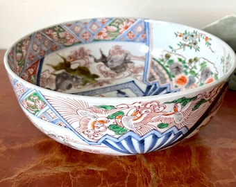 May include: A large, white ceramic bowl with a colorful, intricate design. The bowl features a variety of floral and geometric patterns in shades of blue, red, green, and gold. The bowl is a traditional Japanese style.