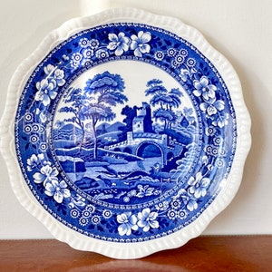 May include: Blue and white ceramic plate with a scalloped edge and a floral design. The center of the plate features a blue and white landscape scene with a bridge and a cottage.
