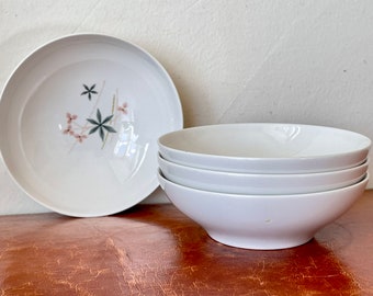 May include: Four white ceramic bowls, three stacked on top of each other. The bowl on the bottom is larger than the other three. The bowl on the left has a floral design in pink and green.