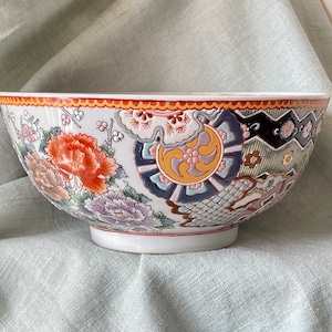 May include: A large white ceramic bowl with a colorful floral and geometric design. The bowl has a wide rim and a rounded bottom.