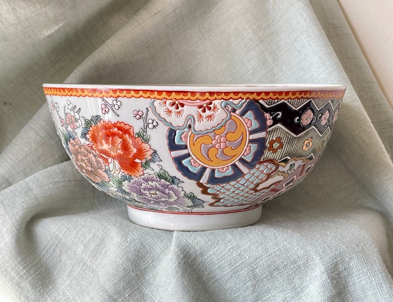 May include: A large white ceramic bowl with a colorful floral and geometric design. The bowl has a wide rim and a rounded bottom.