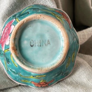 Puede incluir: Un cuenco de cer&aacute;mica azul turquesa con un dise&ntilde;o floral. El cuenco tiene un borde festoneado y est&aacute; marcado con "CHINA" en la parte inferior.