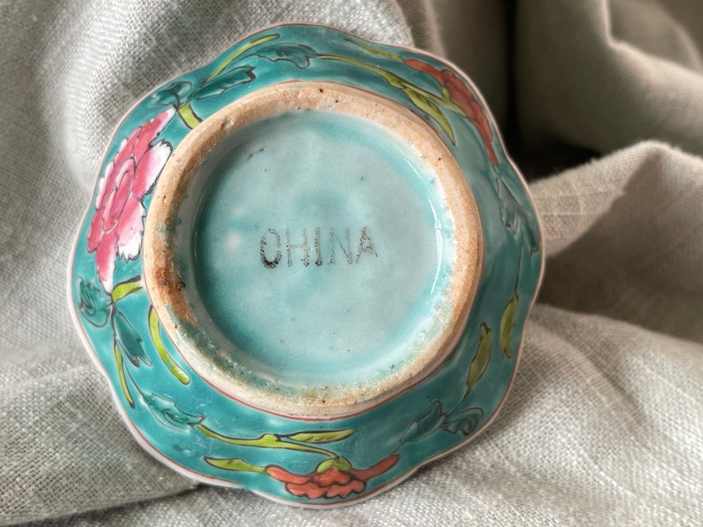 Puede incluir: Un cuenco de cer&aacute;mica azul turquesa con un dise&ntilde;o floral. El cuenco tiene un borde festoneado y est&aacute; marcado con "CHINA" en la parte inferior.