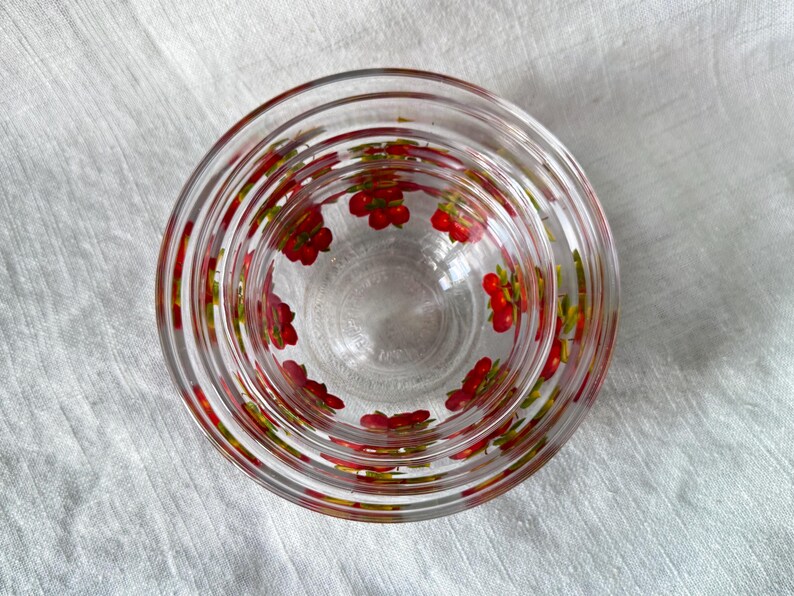 May include: Clear glass bowls, nested, with a red and green floral pattern. The bowls are arranged in a stack, with the smallest bowl inside the largest. The floral pattern is repeated around the rim of each bowl.