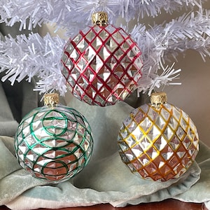 May include: Three glass Christmas ornaments with a mirrored finish. The ornaments are decorated with geometric patterns in red, green, and gold.