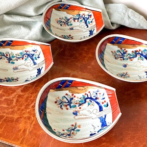 May include: Four decorative ceramic dishes with a unique, asymmetrical shape. Each dish features a white interior with a painted tree design in blue, red, and green. The rims are accented with red and blue stripes, and gold trim.