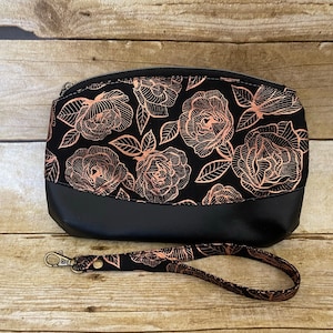 May include: Black zippered pouch with a rose pattern in gold foil. The pouch has a black leather bottom and a detachable strap.