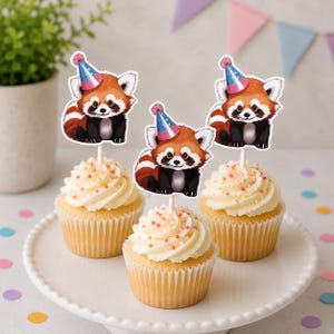 May include: Three cupcakes topped with white frosting and colorful sprinkles, each featuring a red panda cutout wearing a blue and pink party hat. The red pandas have white facial markings, dark eyes, and striped tails, mounted on white sticks.