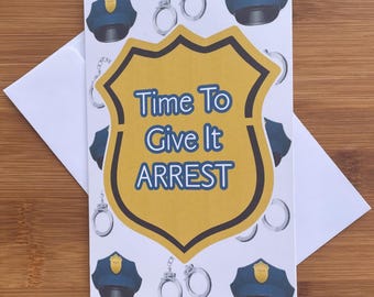 Op de afbeelding: Een witte wenskaart met een herhalend patroon van blauwe politiepetten en zilveren handboeien. In het midden staat een groot goudkleurig schild met de blauwe tekst Time To Give It ARREST. Een effen witte envelop ligt achter de kaart.