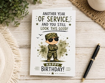 Op de afbeelding: Een witte wenskaart met een cartoon soldaat in camouflage-uniform en zonnebril met gekruiste armen. De tekst luidt: ANOTHER YEAR OF SERVICE, AND YOU STILL LOOK THIS GOOD! HAPPY BIRTHDAY! Het ontwerp bevat groene sterren als accenten.