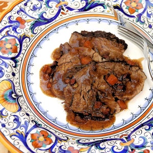 以下が含まれることがあります： 豊かな茶色のグレービーソースとニンジン、ハーブを添えた、スライスされた牛肉のプレートのクローズアップ。プレートはカラフルな花の模様で飾られています。