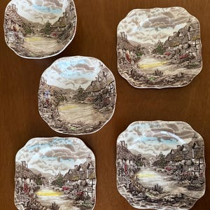 May include: Five vintage decorative plates with a landscape scene. The plates have a square shape with rounded edges. The landscape features a river, houses, and trees, with a cloudy sky. The color palette includes brown, beige, blue, and green.