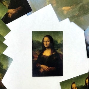 May include: A close-up of a printed image of the Mona Lisa painting. The image is surrounded by other smaller images of the Mona Lisa, all printed on a white background.