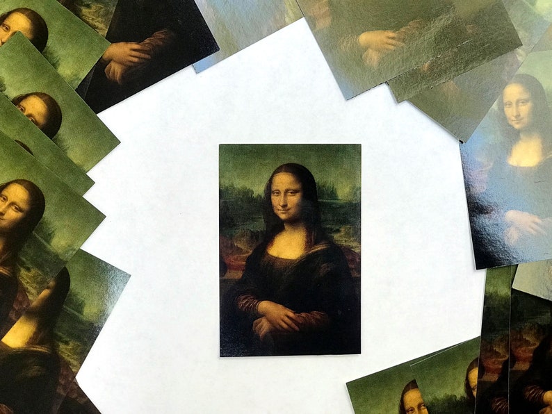 May include: A close-up of a printed image of the Mona Lisa painting. The image is surrounded by other smaller images of the Mona Lisa, all printed on a white background.
