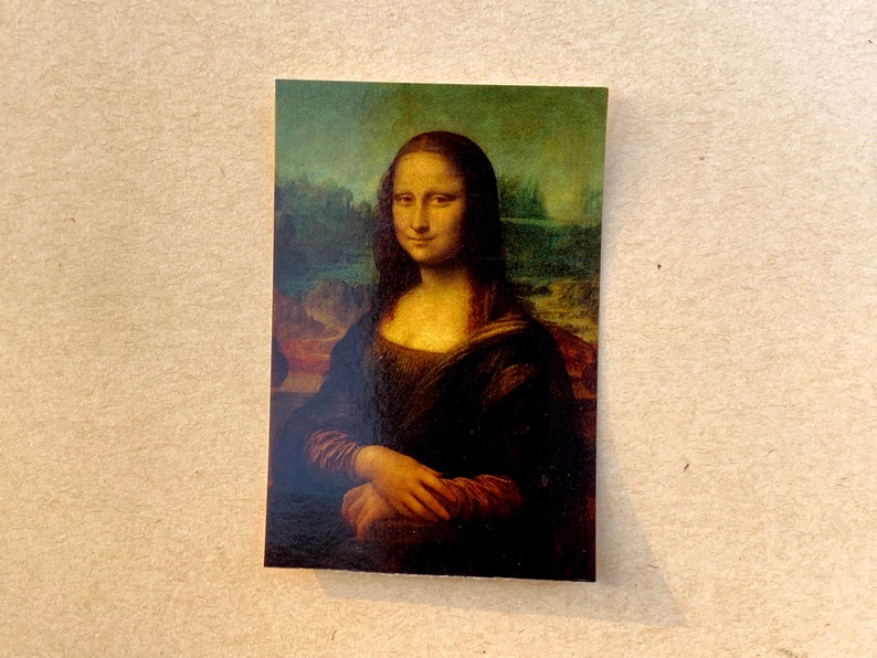 May include: A close-up of the Mona Lisa painting, a famous portrait of a woman with a mysterious smile. The painting is set against a landscape background with a rocky outcropping and a body of water.