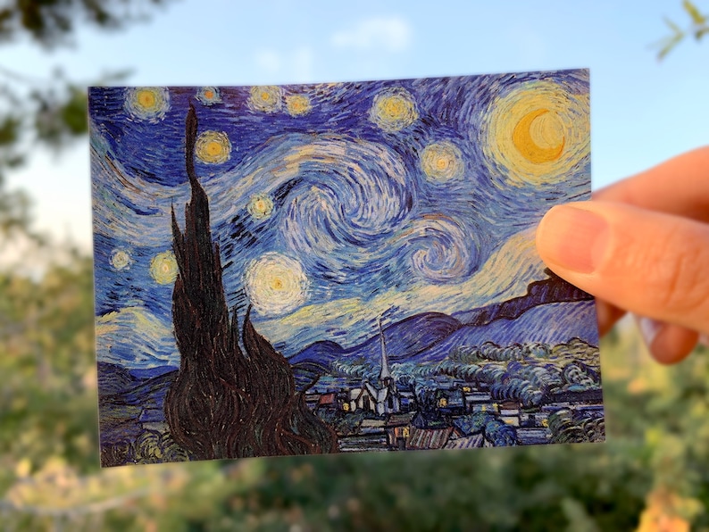 Puede incluir: Una postal con una reproducci&oacute;n de la famosa pintura de Vincent van Gogh, "La noche estrellada". La pintura representa un cielo nocturno en espiral con una luna amarilla brillante y estrellas, y un peque&ntilde;o pueblo en primer plano.