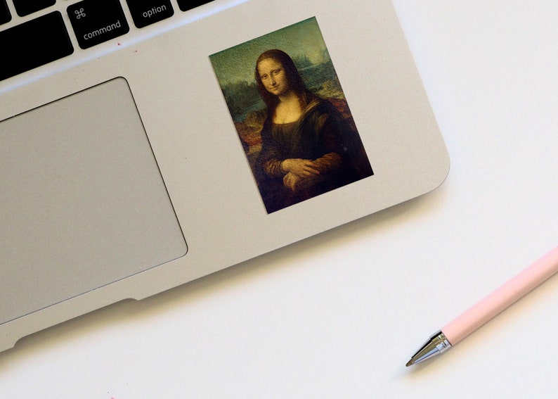 May include: A sticker featuring a painting of the Mona Lisa, a famous portrait by Leonardo da Vinci. The sticker is on a silver laptop.