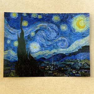 Puede incluir: Una pintura de un cielo nocturno estrellado con una gran luna amarilla giratoria en la esquina superior derecha. El cielo es de un azul profundo con estrellas blancas y un &aacute;rbol alto y oscuro en primer plano. Hay peque&ntilde;as casas blancas en la distancia.