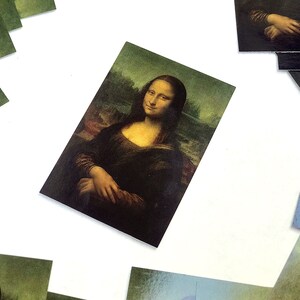 May include: A set of postcards featuring a reproduction of the famous Mona Lisa painting. The postcards are printed on high-quality cardstock and feature a glossy finish.
