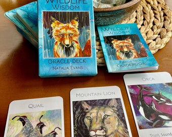 Può includere: Un set di carte oracle con illustrazioni colorate di animali, tra cui una quaglia, un leone di montagna e un'orca. Le carte fanno parte di un mazzo chiamato "Wildlife Wisdom Oracle Deck" di Natalia Evans. Ogni carta presenta una descrizione del significato dell'animale, come "Unità, Equilibrio, Rete della Vita" per la carta della quaglia.