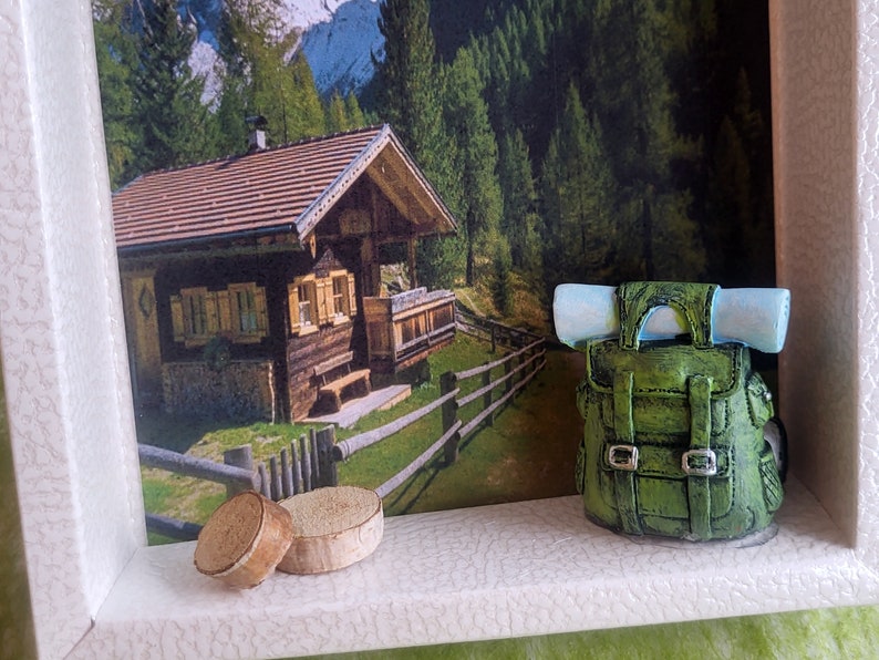 May include: A miniature wooden cabin with a red roof and a green backpack with a blue roll on top, sitting on a shelf with two wooden discs.