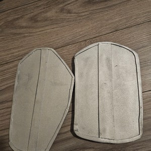 May include: Two silver-colored, foam-backed, armor pieces for cosplay or costume making.