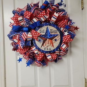 Op de afbeelding: Een rood, wit en blauwe patriottische krans met een stervormig bord met de tekst "God Bless U.S.A."