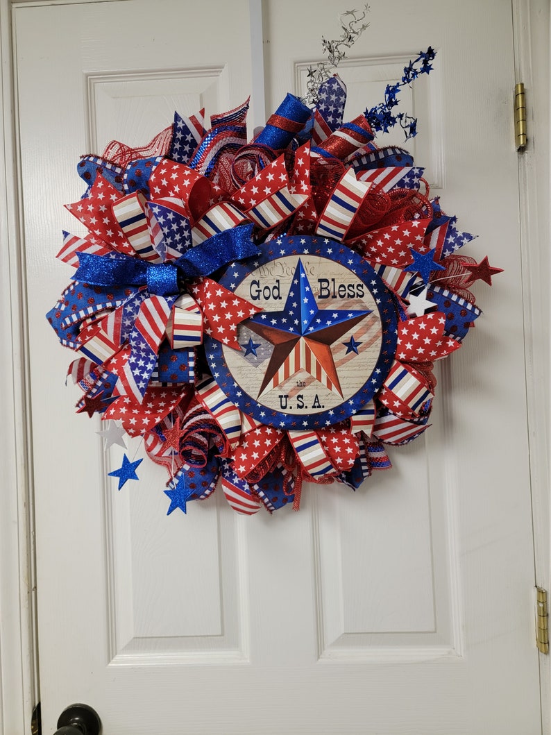 Op de afbeelding: Een rood, wit en blauwe patriottische krans met een stervormig bord met de tekst "God Bless U.S.A."