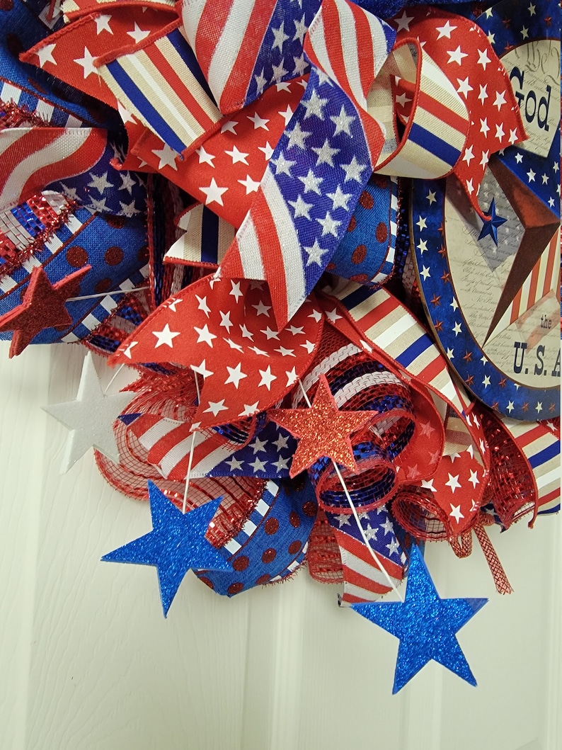 Op de afbeelding: Een rood, wit en blauwe patriottische krans met sterren, strepen en een bord met de tekst "We the People, In God We Trust, U.S.A."