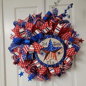 Op de afbeelding: Een rood, wit en blauwe patriottische krans met een stervormig bord met de tekst "God Bless the U.S.A."