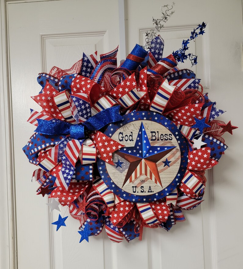 Op de afbeelding: Een rood, wit en blauwe patriottische krans met een stervormig bord met de tekst "God Bless the U.S.A."