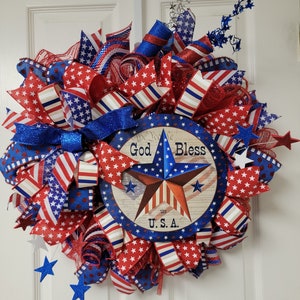 Op de afbeelding: Een rood, wit en blauwe patriottische krans met een bord waarop staat "God Bless the U.S.A."