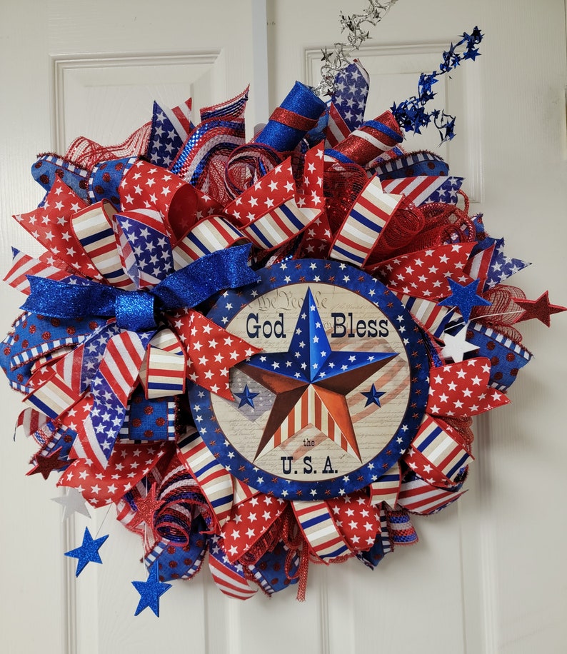 Op de afbeelding: Een rood, wit en blauwe patriottische krans met een bord waarop staat "God Bless the U.S.A."