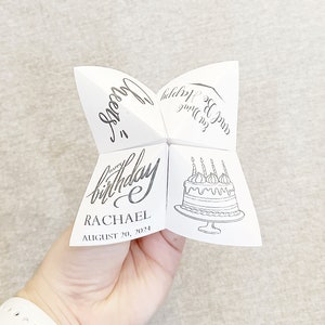 hand holding white paper cootie catcher against gray background