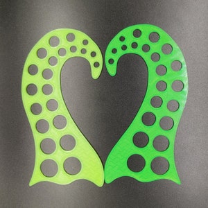 May include: Two green, heart-shaped objects with numerous circular cutouts. The objects have a wavy design and are arranged to form a heart shape. The color is a vibrant green, and the objects appear to be made of plastic or a similar material.