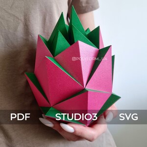 May include: A pink and green geometric papercraft sculpture in the shape of a flower. The sculpture is being held by a person's hand. The text "STUDIO3" is visible on the sculpture.
