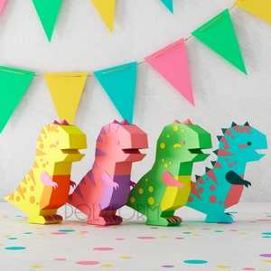 May include: Four colorful paper dinosaur figures stand in a row on a white surface with confetti. The dinosaurs are yellow, pink, green, and blue.