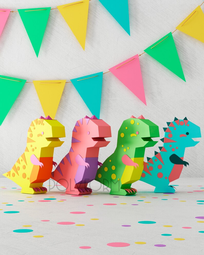 May include: Four colorful paper dinosaur figures stand in a row on a white surface with confetti. The dinosaurs are yellow, pink, green, and blue.