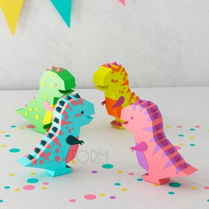 May include: Four papercraft dinosaurs in different colors: green, blue, yellow, and pink. The dinosaurs are standing on a white surface with colorful confetti.