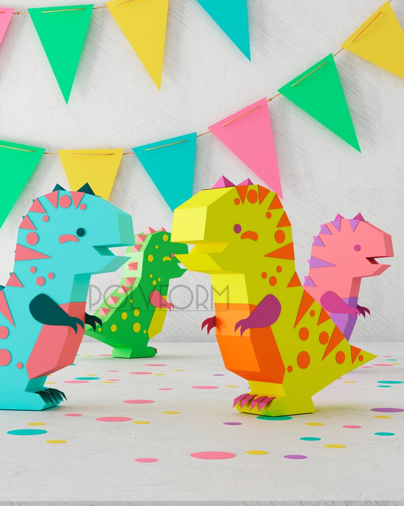 May include: Three papercraft dinosaurs in blue, green, and pink with yellow, orange, and purple accents. The dinosaurs are standing on a white surface with confetti.