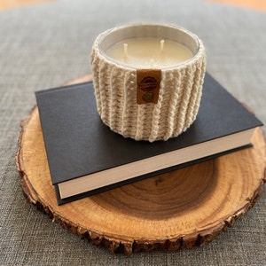 K&ouml;nnte beinhalten: Ein wei&szlig;er geh&auml;kelter Kerzenhalter mit einem braunen Leder-Etikett mit der Aufschrift "Wild Spirit" auf einem schwarzen Buch und einer Holzscheibe.