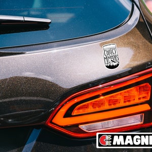 Puede incluir: Un coche negro con una pegatina blanca en la parte trasera. La pegatina es un tarro de cristal con las palabras "Collect Memories" escritas en &eacute;l. El coche tiene una luz trasera roja y una etiqueta negra "MAGNET" en la parte inferior.