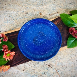 May include: A blue speckled ceramic plate with a floral design. The plate is on a wooden surface with a light brown background.