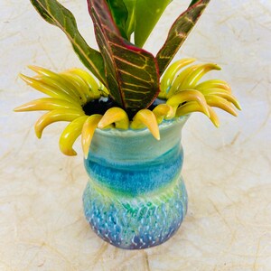 May include: A blue and green ceramic vase with a wavy design. The vase has a yellow flower-like design around the top.