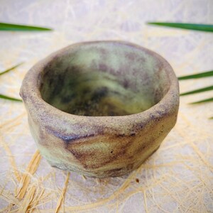 May include: A small, green and brown ceramic bowl with a rough, textured surface. The bowl is empty and has a slightly rounded shape.