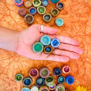 May include: A collection of small, colorful ceramic bowls. The bowls are various shades of green, blue, brown, and yellow. Some of the bowls have a speckled or textured finish.